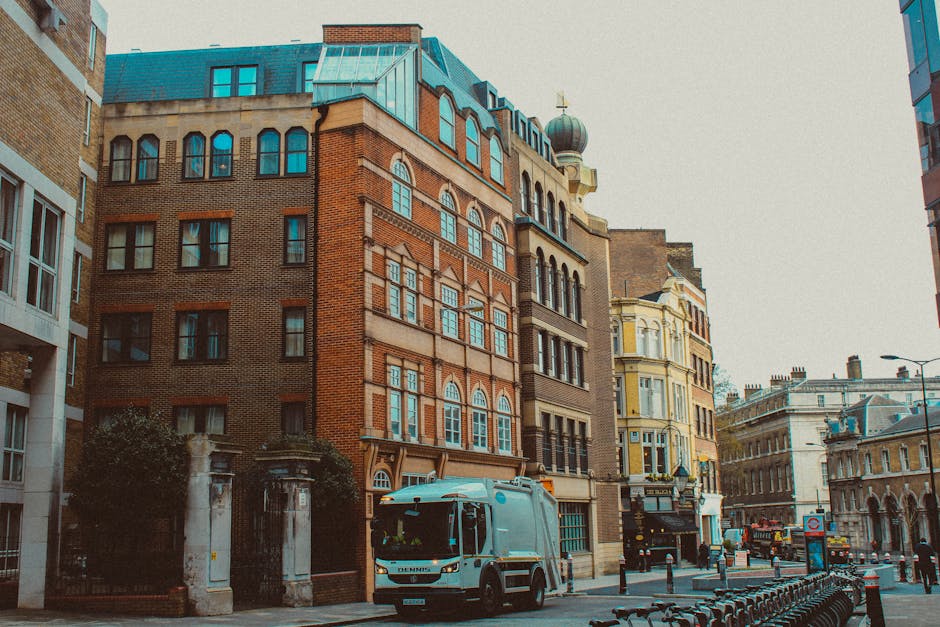 A team of professional movers from Storage Wandsworth are in the process of loading cardboard boxes and wrapped furniture onto a large moving van outdoors, with one worker carrying a box and another s